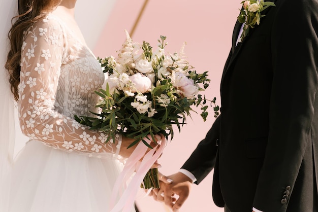 Un lussuoso bouquet da sposa con peonie nelle mani degli sposi