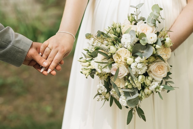 Un lussuoso bouquet da sposa con rose bianche nelle mani degli sposi