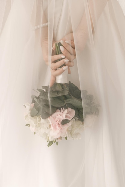 Un lussuoso bouquet da sposa con rose bianche nelle mani della sposa sotto un velo