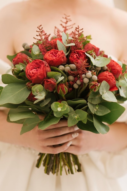 Un lussuoso bouquet da sposa con rose rosse nelle mani della sposa