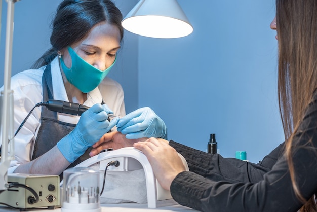 Un maestro di manicure donna nel salone in procinto di lavorare con le unghie del cliente su uno sfondo blu