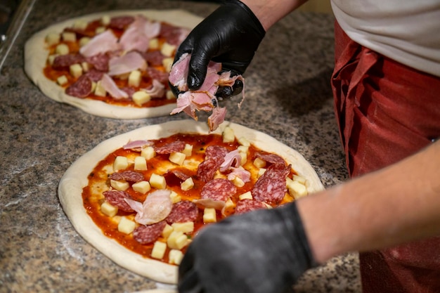 Un maestro pizzaiolo in mascherina e guanti stende gli ingredienti sulla pizza