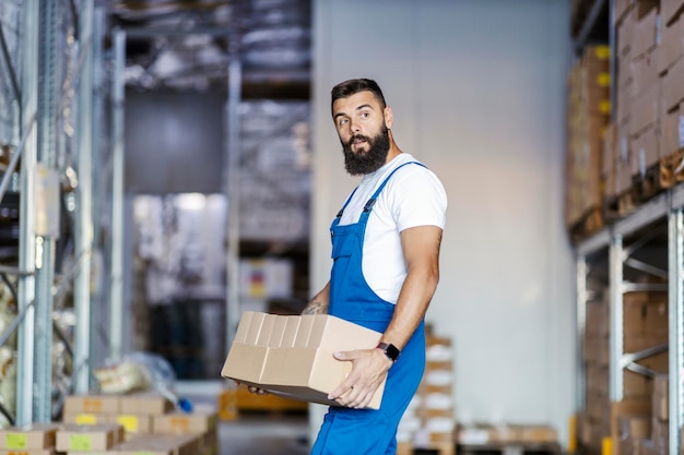 Un magazziniere forte e muscoloso in tuta sta trasferendo scatole da un posto all'altro