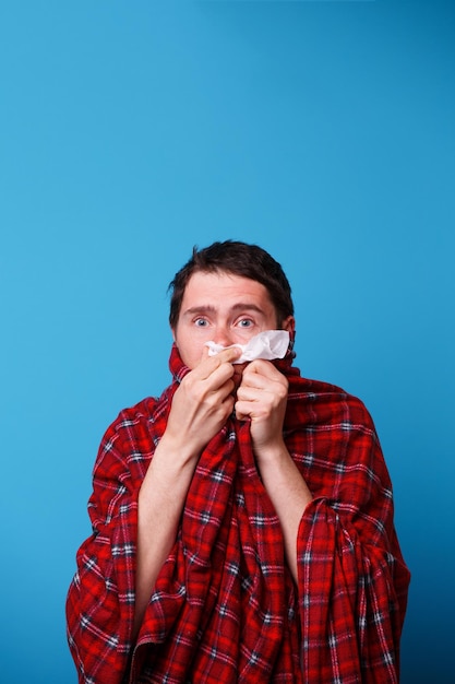 Un malato avvolto in una coperta si soffia il naso in un fazzoletto bianco