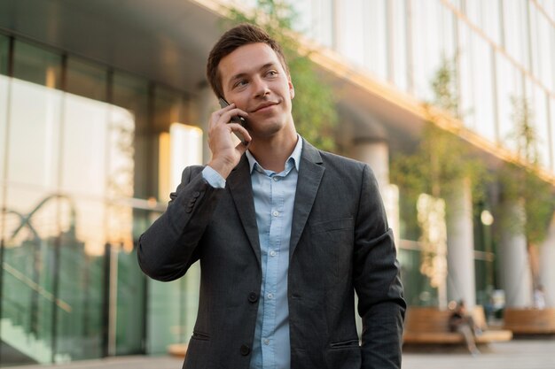 Un manager dell'uomo d'affari sta chiamando al telefono in piedi vicino all'ufficio in giacca e cravatta Ritratto di un finanziere in attesa di un collega sul progetto