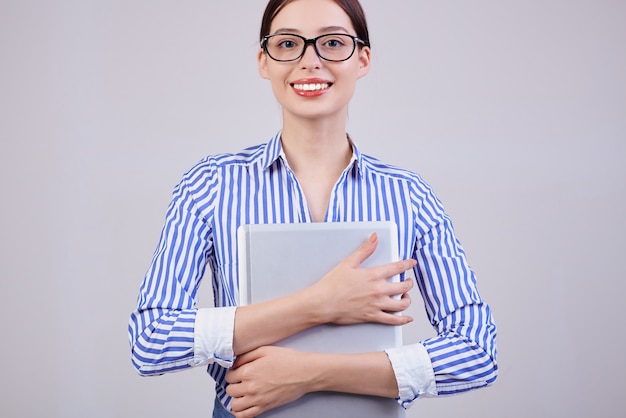 Un manager donna guarda dritto con un sorriso in una camicia a righe bianco-blu con occhiali neri e un computer portatile