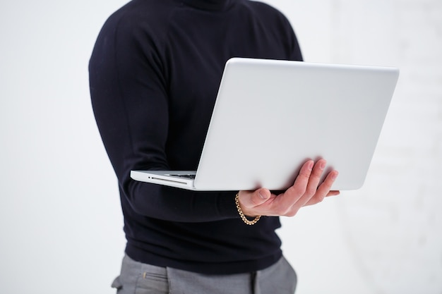 Un manager uomo d'affari sorride e sta in piedi con un laptop in mano e guarda lo schermo. Si erge su uno sfondo bianco.