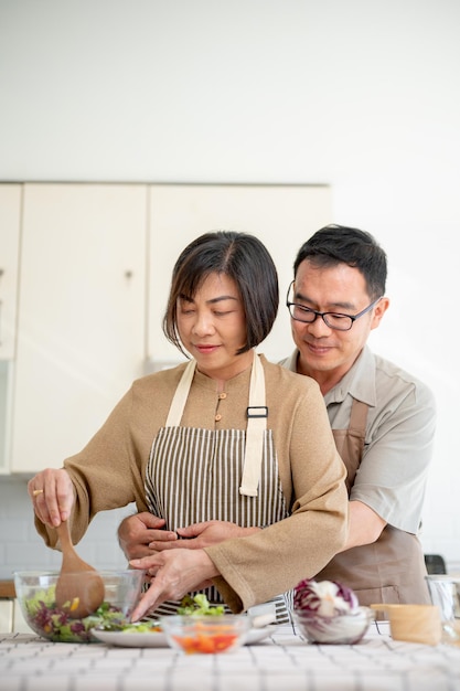 Un marito asiatico romantico e premuroso sta abbracciando sua moglie da dietro mentre cucina