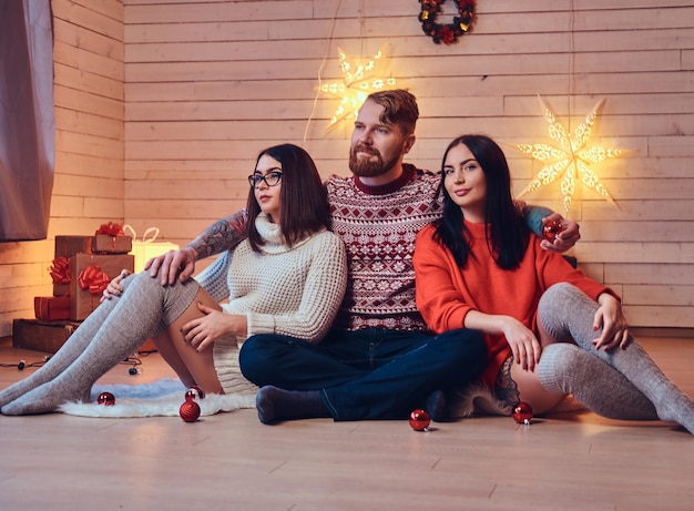 Un maschio barbuto e due donne castane Festa di Natale sopra la parete di legno bianca.