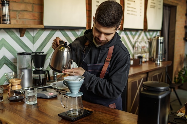 Un maschio barista produce una tazza di caffè e un impiegato del caffè prepara una tazza di caffè con un sistema unico.