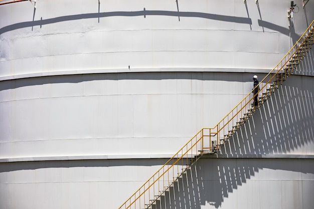 Un maschio che cammina lungo le scale dell'olio del serbatoio di stoccaggio della registrazione visiva dell'ispezione al piano superiore sulla piastra laterale