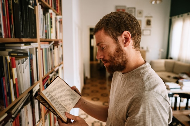 Un maschio dalla testa rossa che legge un libro nella biblioteca di casa