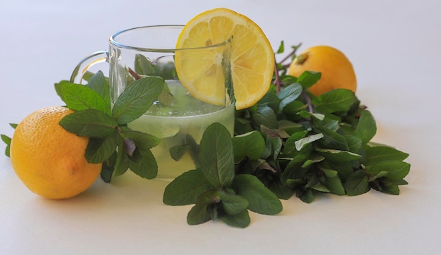 Un mazzo di erbe fresche di menta su sfondo bianco, limone e succo di limone in un bicchiere.Tonico.