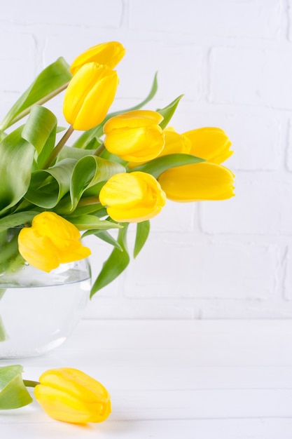 Un mazzo di fiori di tulipano giallo in vaso di vetro su sfondo bianco. Un regalo per la festa di una donna. Copia spazio.