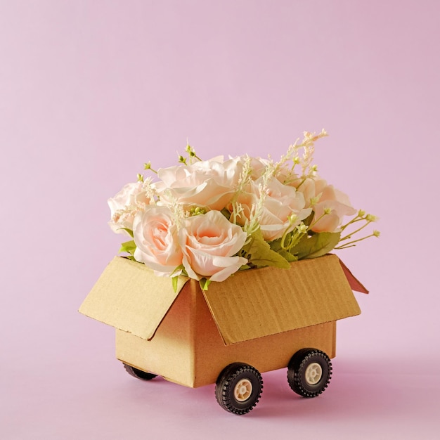 Un mazzo di fiori in fiore di romantiche rose rosa come regalo in una scatola di consegna con ruote di camion