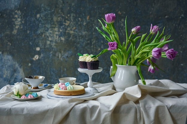 Un mazzo di fiori, torte, cupcakes e una tazza di tè sul tavolo