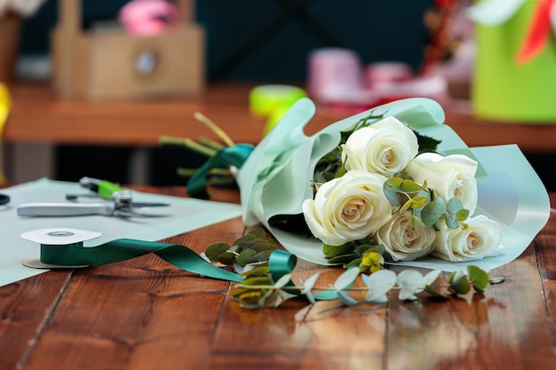 Un mazzo di rose bianche in imballaggi di carta giace su un tavolo di legno.