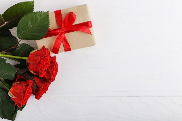 Un mazzo di rose rosse, un regalo su un tavolo di legno bianco