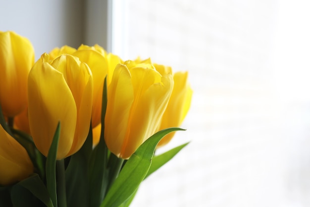 Un mazzo di tulipani gialli freschi in un vaso su un tavolo vicino alla finestra