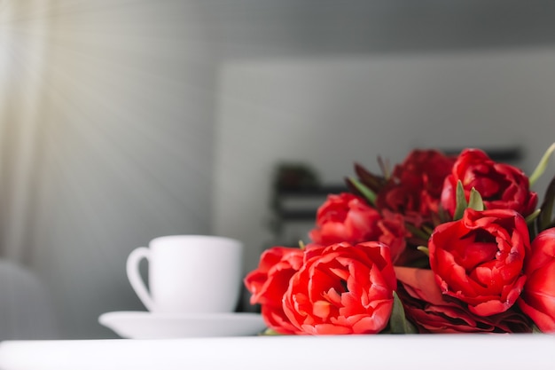 Un mazzo di tulipani rossi sul tavolo e una tazza di caffè bianca.