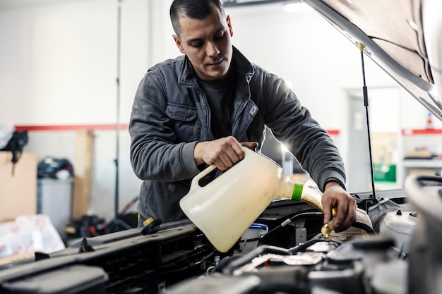 Un meccanico automobilistico sta versando olio nel motore dell'auto sotto il cofano mentre si trova in garage