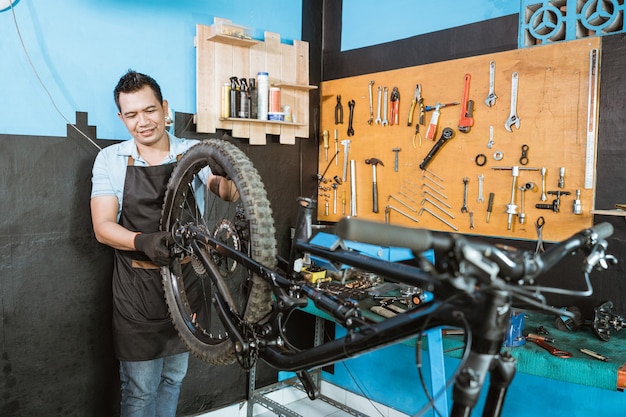 Un meccanico di biciclette in grembiule installa le ruote durante l'assemblaggio di un telaio di bicicletta