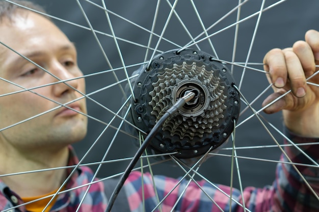 Un meccanico di biciclette tiene una ruota di una bicicletta Riparazione di biciclette Raggi delle ruote e cassetta di una mountain bike su sfondo nero