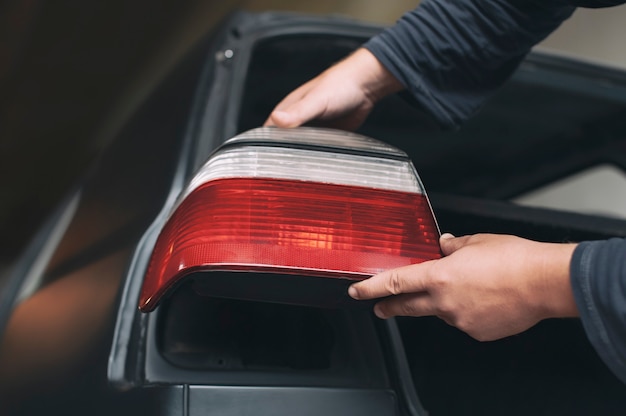 Un meccanico installa i fanali posteriori in una nuova auto presso un servizio di auto. Un uomo tiene in mano un faro.