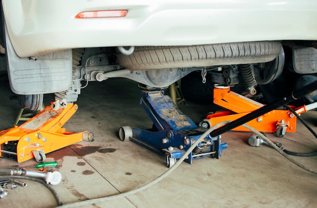 Un meccanico solleva un'auto con tre martinetti in un garage di riparazione auto per verificare il problema Concetto di servizio di manutenzione auto