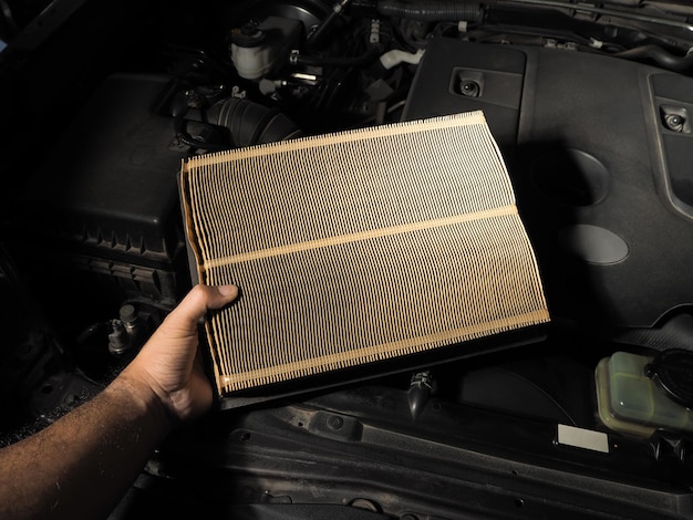 Un meccanico tiene in mano un filtro dell'aria per auto per la manutenzione automatica in un'officina