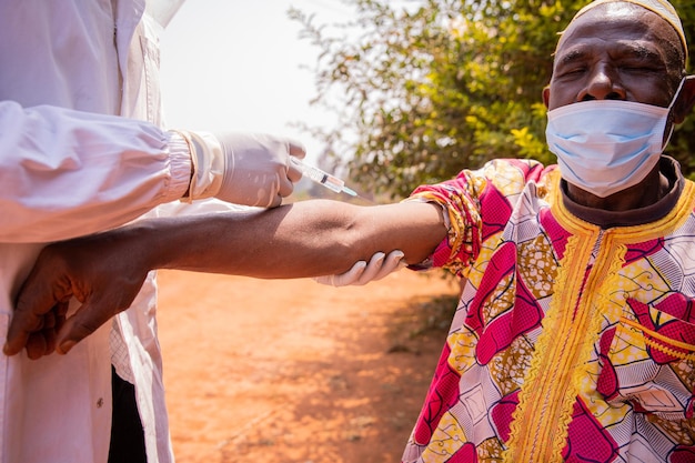 Un medico africano vaccina un anziano con una siringa sul braccio