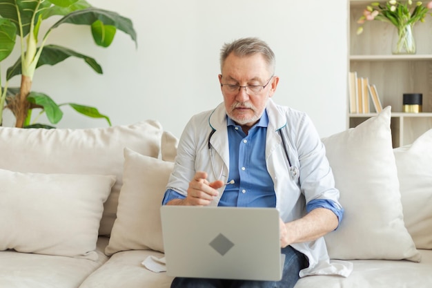 Un medico anziano con un laptop parla su videochiamata ha una consultazione con un paziente professionista anziano