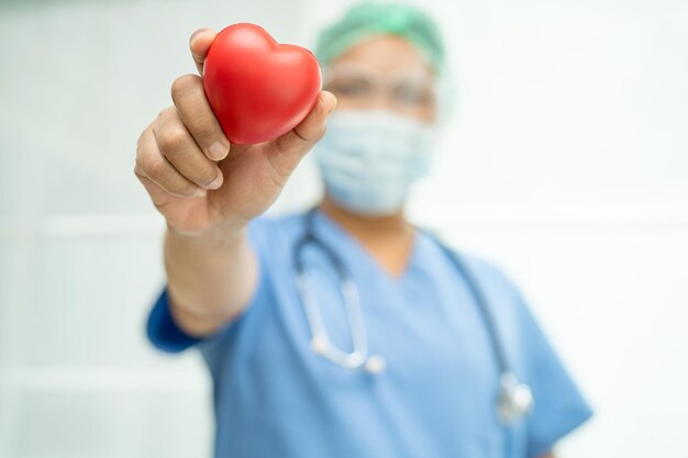 Un medico asiatico indossa un maschera e un abito PPE, la nuova normalità per proteggere dall'infezione da Covid-19 Coronavirus, con un cuore rosso in mano in ospedale