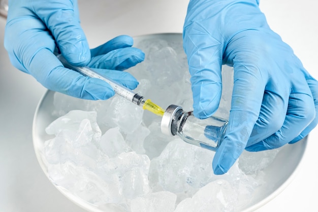Un medico che prende una fiala di vaccino dal frigorifero freddo e prepara l'iniezione. Fiale sul ghiaccio. Conservazione a lungo termine del vaccino Covid-19. Fiale di vaccino contro il coronavirus conservate a temperatura di cella frigorifera