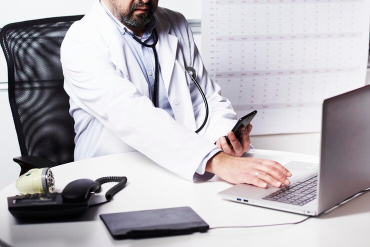 Un medico consulta sul suo cellulare la conferma della password e digita sul suo laptop