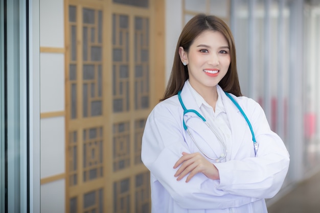Un medico donna asiatica in piedi con le braccia incrociate. Indossa una veste bianca e uno stetoscopio