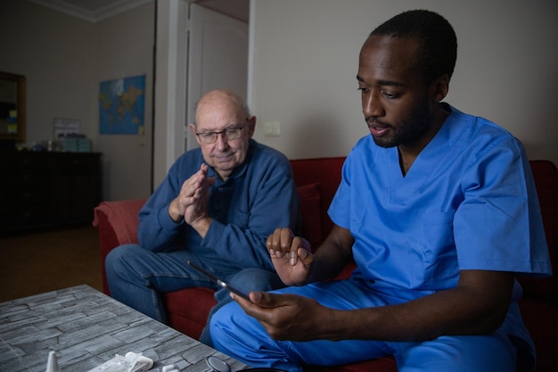 Un medico durante una visita domiciliare con il suo paziente utilizza il tablet digitale