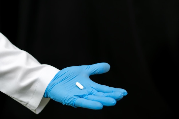 Un medico in camice bianco tiene in mano una pillola su sfondo nero Preparativi medici per il trattamento del coronavirus Un giovane medico stagista sta valutando un nuovo farmaco