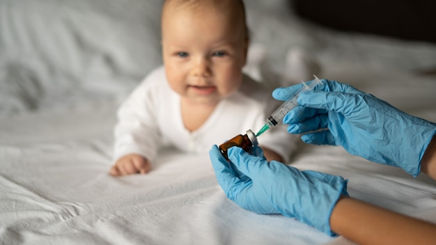 Un medico in guanti blu tiene una siringa in un'ampolla per la vaccinazione sullo sfondo di un bambino, un bambino, su uno sfondo chiaro.