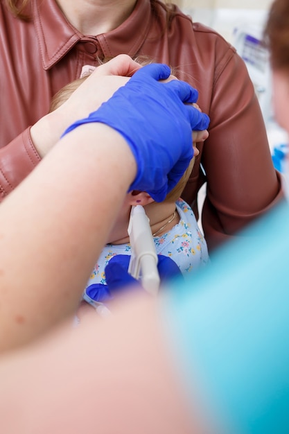 Un medico infermiere trafigge le orecchie di una bambina di otto mesi. Bellezza per i bambini piccoli