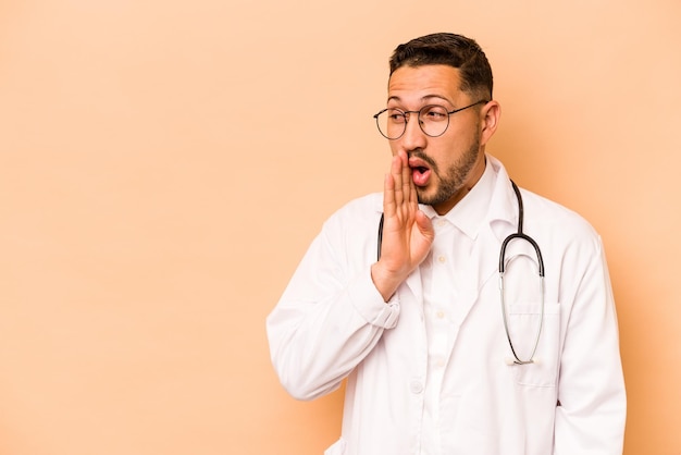 Un medico ispanico isolato su sfondo beige sta dicendo una notizia segreta di frenata calda e sta guardando da parte