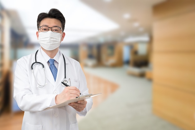 Un medico maschio asiatico in possesso di un diagramma medico in ospedale mentre indossa una maschera.