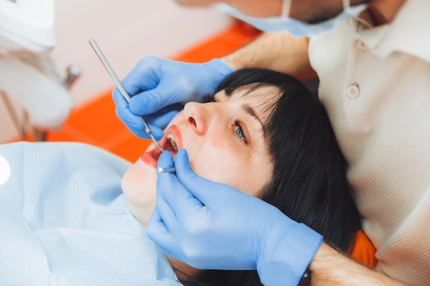 Un medico maschio esamina la cavità orale di un giovane paziente seduto sulla poltrona di un dentista nell'ufficio accanto al dentista il concetto di denti sani