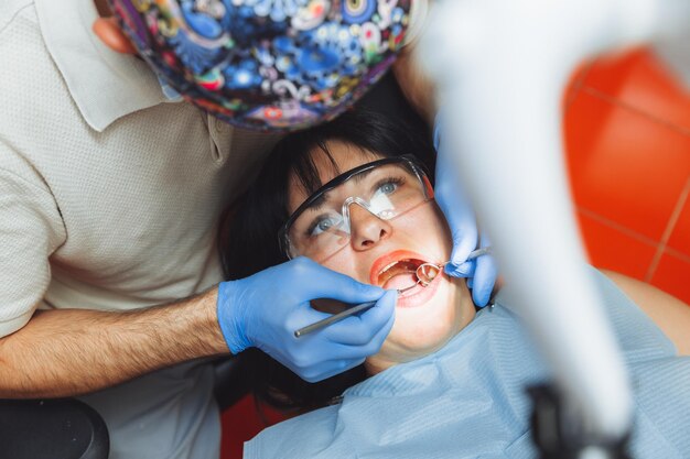 Un medico maschio esamina la cavità orale di un giovane paziente seduto sulla poltrona di un dentista nell'ufficio accanto al dentista il concetto di denti sani