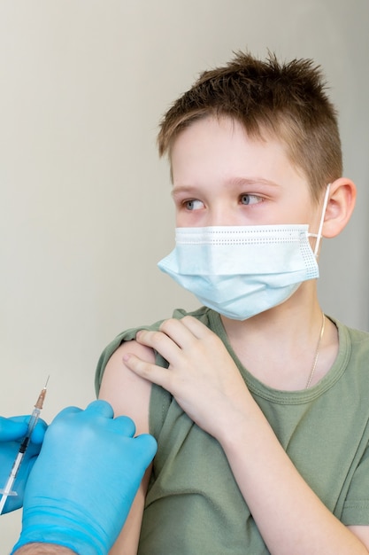 Un medico maschio in una maschera protettiva e con uno stetoscopio vaccina un bambino