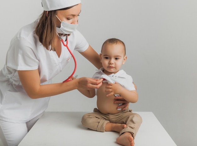 Un medico per bambini esamina un bambino di un anno con uno stetoscopio in un centro ospedaliero. concetto di salute