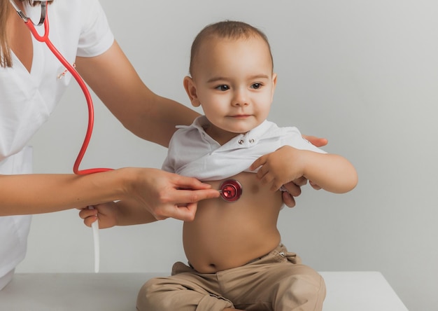 Un medico per bambini esamina un bambino di un anno con uno stetoscopio in un centro ospedaliero. concetto di salute