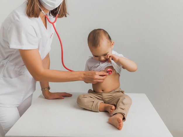 Un medico per bambini esamina un bambino di un anno con uno stetoscopio in un centro ospedaliero. concetto di salute