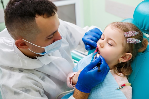 Un medico professionista, un dentista per bambini, cura i denti di una bambina con degli strumenti. Studio dentistico per l'esame del paziente. Il processo di trattamento dentale in un bambino