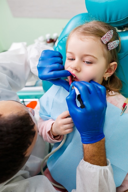 Un medico professionista, un dentista per bambini, cura i denti di una bambina con degli strumenti. Studio dentistico per l'esame del paziente. Il processo di trattamento dentale in un bambino